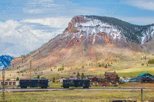 Train cars on track in front of houses in Silverton Colorado with mountains with snow in background. photo