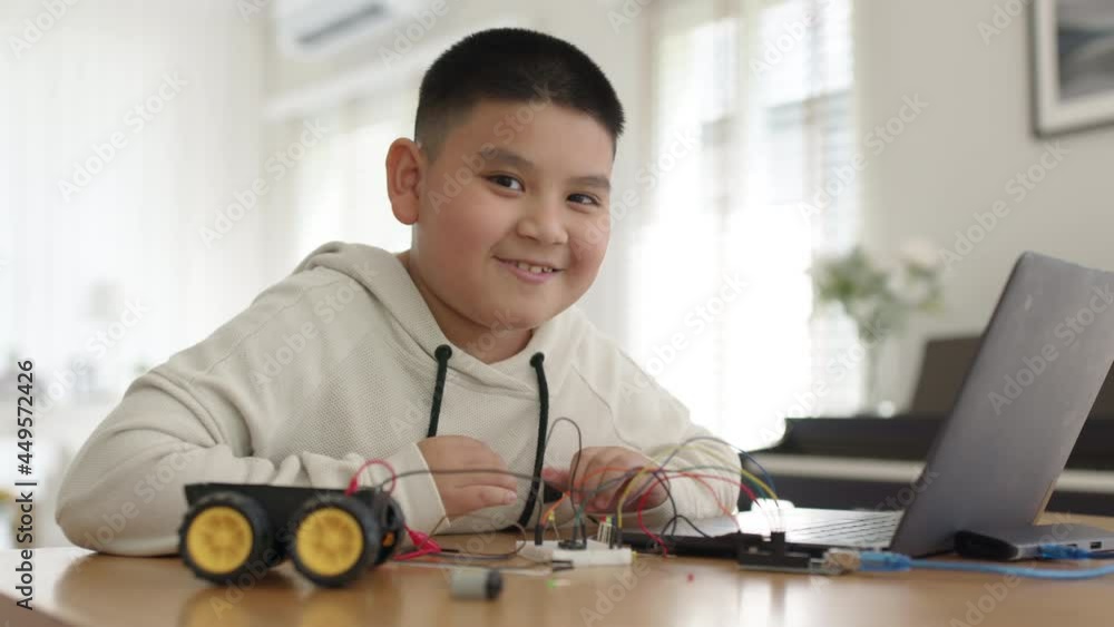 Young asia teen people smile with pride look at camera sitting at home remote learn online tutor training course at desk table enjoy making electrical robot build cable car. Kid boy play in fun class. Young asia teen people smile with pride look at camera sitting at home remote learn online tutor training course at desk table enjoy making electrical robot build cable car. Kid boy play in fun class.