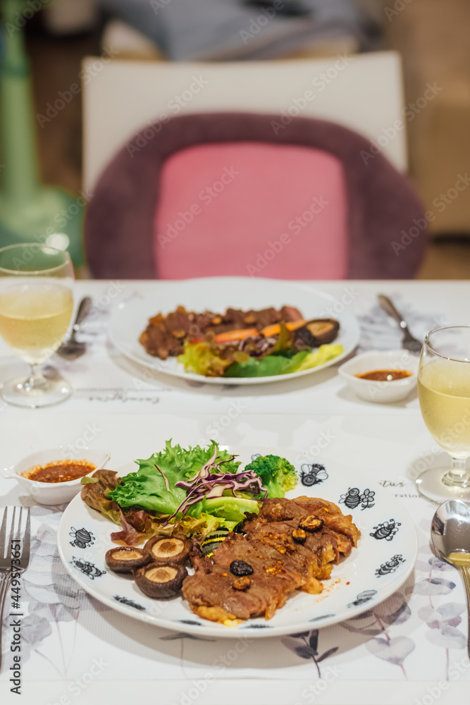 grilled ribeye beef black pepper steak with salad mushroom and green vegetable on white plate and two glass of white wine. grilled ribeye beef black pepper steak with salad mushroom and green vegetable on white plate and two glass of white wine.