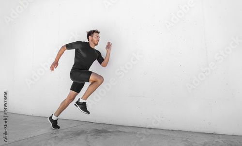 Sport athlete training running fast with explosive sprint for competition. Man runner working out at fitness gym outdoor white wall background.