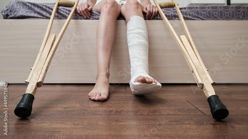 Woman with broken leg sitting on the bed and holding crutches