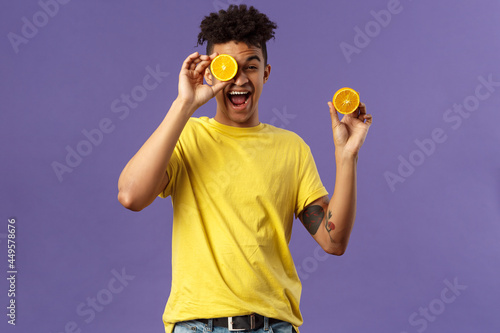 Holidays, vitamins and vacation concept. Portrait of carefree, upbeat good-looking man having fun, look playful laughing, likes eating fruits healthy food, holding pieces of oranges