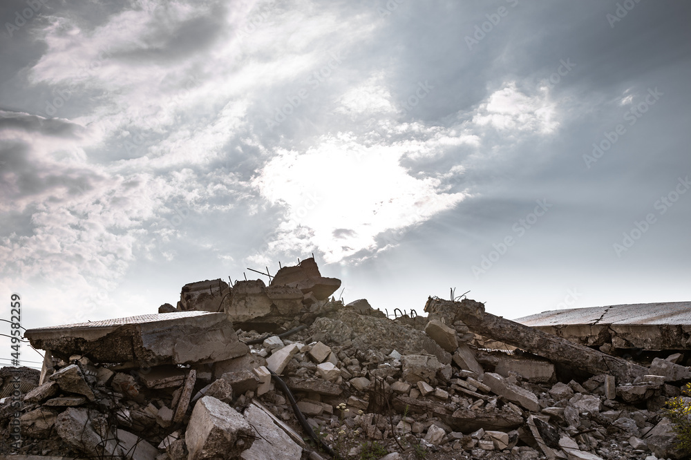 A pile of construction debris made of concrete fragments of slabs, beams and bricks against the background of a sunny grey sky. Background A pile of construction debris made of concrete fragments of slabs, beams and bricks against the background of a sunny grey sky. Background