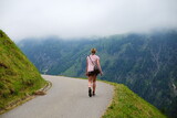 Junge Frau wandert auf enger Straße in den Bergen vor nebelverhangener Landschaft