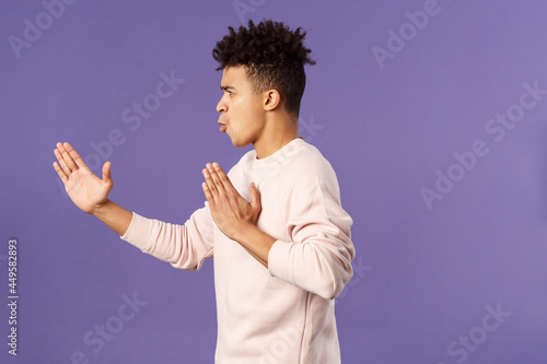 Profile portrait of young hispanic guy with dreads acting like he is ninja or martial arts fighter, practice his kung-fu or taekwondo skills, standing purple background