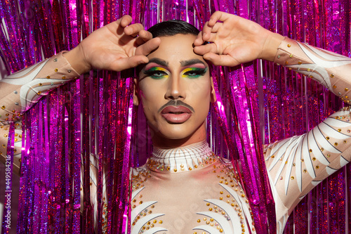 portrait of beautiful young man in drag queen makeup looking at camera and colorful background photo