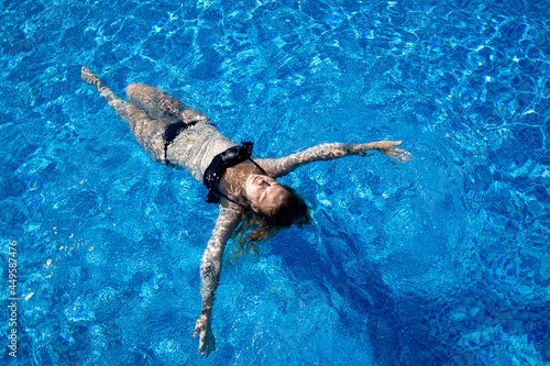 girl with a beautiful figure swims on her back on the water in the pool top view