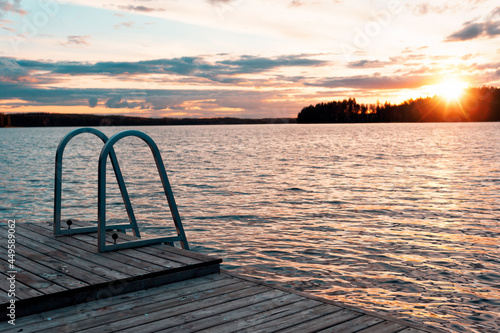 Stairs into a lake during sunset. Wooden swimming pier with metal ladders.