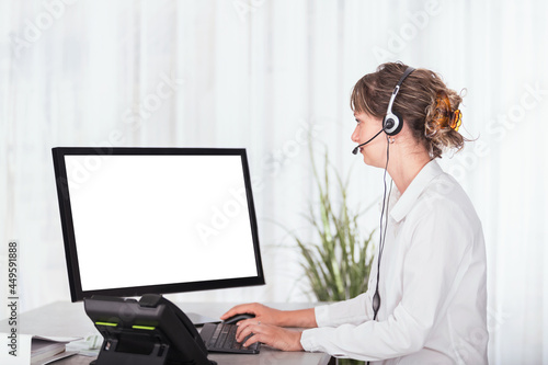 Side view of a woman with headset in the office using computer and looking to blank screen to copy space