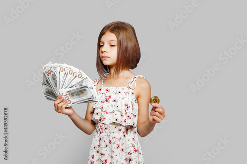 Beautiful little girl holding virtual currency bitcoin and dollars perplexedly don't know what to choose to invest future photo