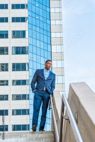 A young handsome black businessman is standing outside of a business building, relaxing and thinking.. © Alexander Image
