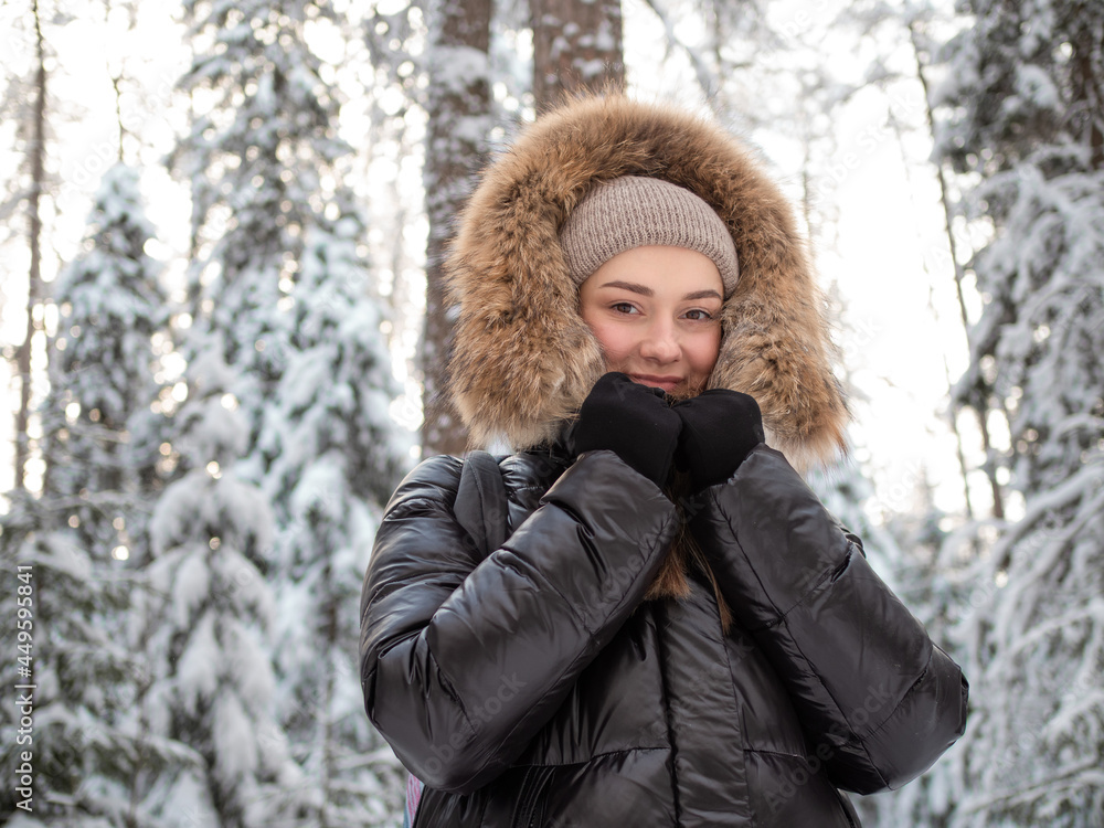 young woman in a winter down jacket with fur hood walks in the forest in winter young woman in a winter down jacket with fur hood walks in the forest in winter