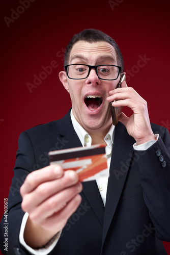 Down syndrome businessman talking on his phone with bank, stunned by his credit card balance