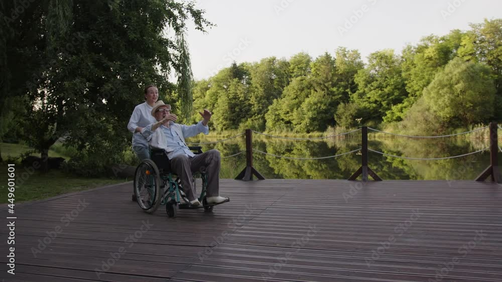 Nurse and old patient walk near the park lake Nurse and old patient walk near the park lake