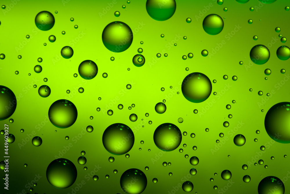Abstract green background with water drops on the glass. A fogged beer bottle in close-up.
