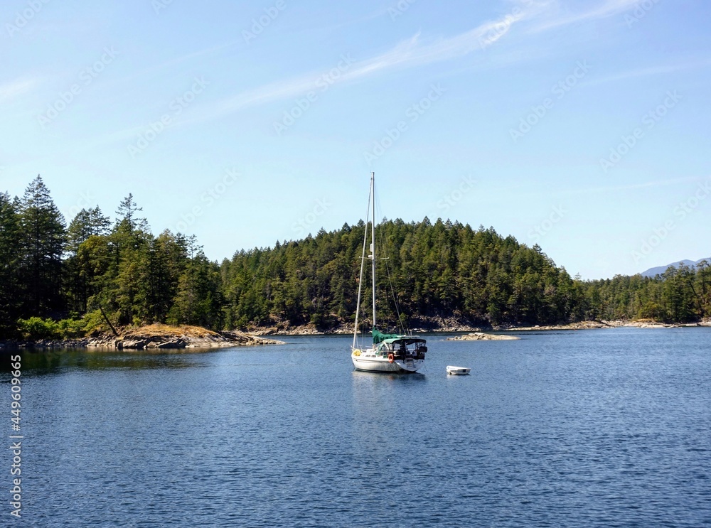 An isolated photo of a medium sized sailboat in a bay surrounded by beautiful forests, on a sunny day with blue sky, in ballet bay, on the sunshine coast, british columbia, canada
