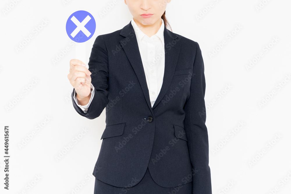 白背景の前に立って、NGのジェスチャーをするスーツを着たビジネスウーマン