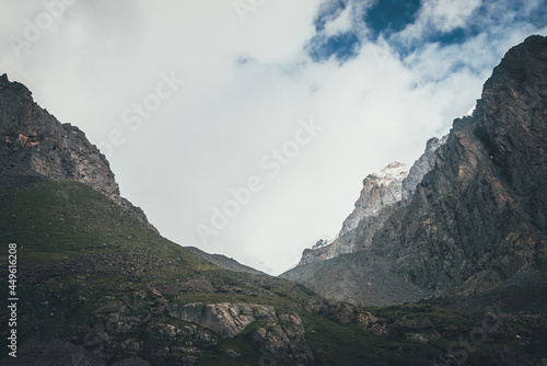 Atmospheric mountain landscape with narrow valley among high rocky mountains and low clouds. Beautiful mountain valley under cloudy sky. Awesome scenery with glen among sharp rocks. Unimaginable view.