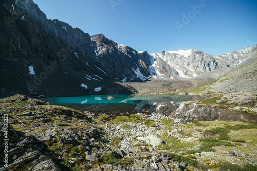 Snowy mountain reflected in clear water of glacial lake. Beautiful sunny landscape with glacier reflection in water surface of mountain lake under clear sky. Snow on rock reflected in mountain lake.