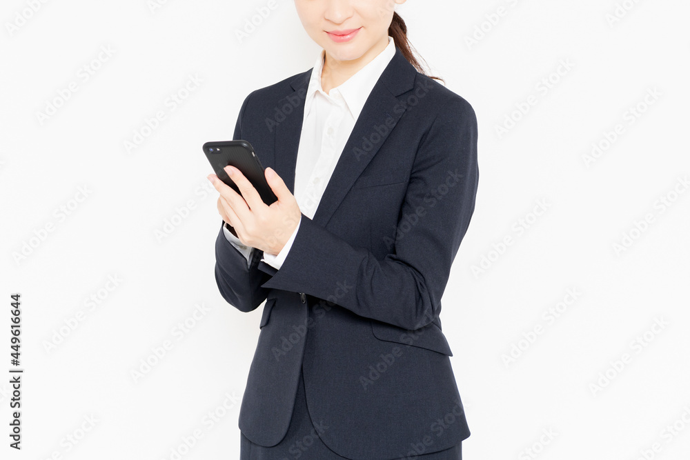 白背景の前に立って、スマホを操作するスーツを着たビジネスウーマン