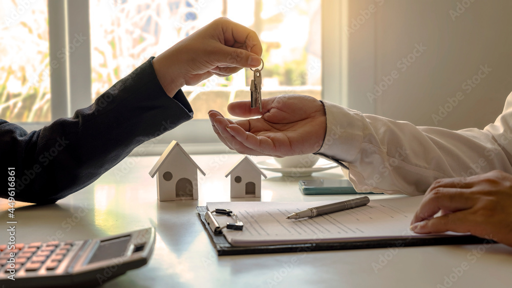 The real estate agent provides the house keys to the customer after signing the real estate contract with an approved mortgage request form. home mortgage loan concept and home insurance The real estate agent provides the house keys to the customer after signing the real estate contract with an approved mortgage request form. home mortgage loan concept and home insurance