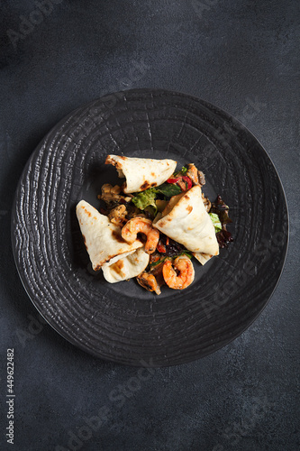Salad with shrimp and pita bread. Seafood and vegetable on black ceramic plate.  Gourmet, restaurant healthy food concept. Dark textured table