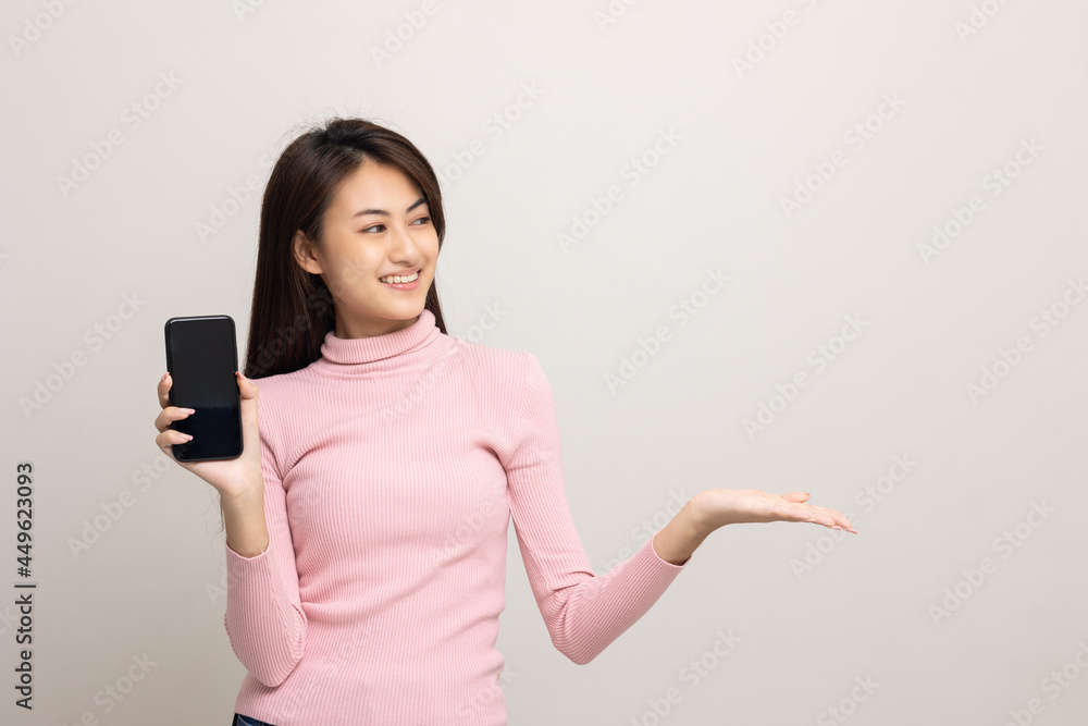 Pretty young asian woman showing screen of smartphone and palm up hand holding something standing on isolated white background. She very happy. Pretty young asian woman showing screen of smartphone and palm up hand holding something standing on isolated white background. She very happy.
