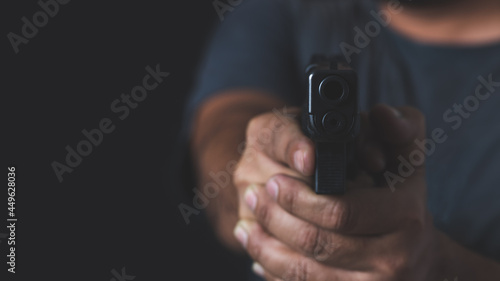 Man holding a gun in his hand with a black background.