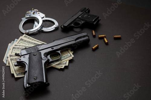 Pistol handcuffs and American dollar banknotes on black background.