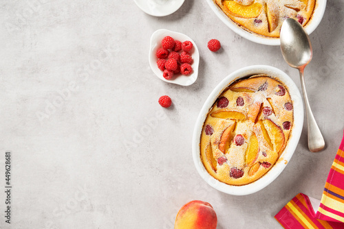 Traditional french pie clafoutis with fresh summer peaches and raspberry. Light- gray stone background, top view