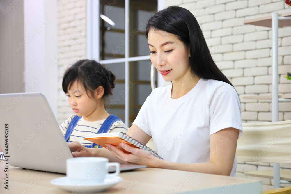 Asian mother working online from home using laptop while watching her daughter working on assignment from school for homeschooling and education concept Asian mother working online from home using laptop while watching her daughter working on assignment from school for homeschooling and education concept