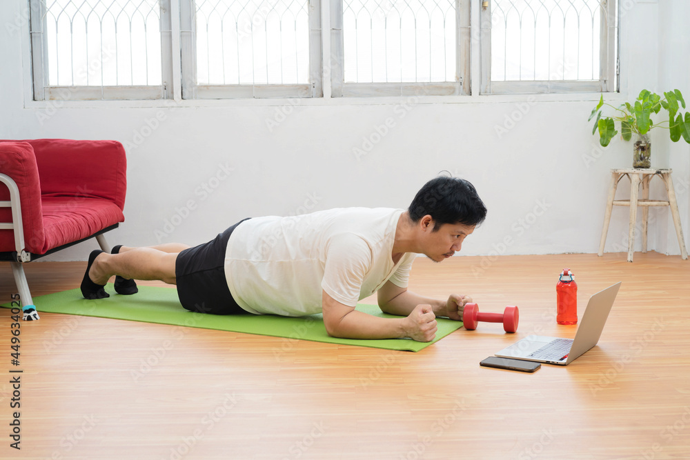 Online workout. Young man doing plank exercise with online tutorial at home