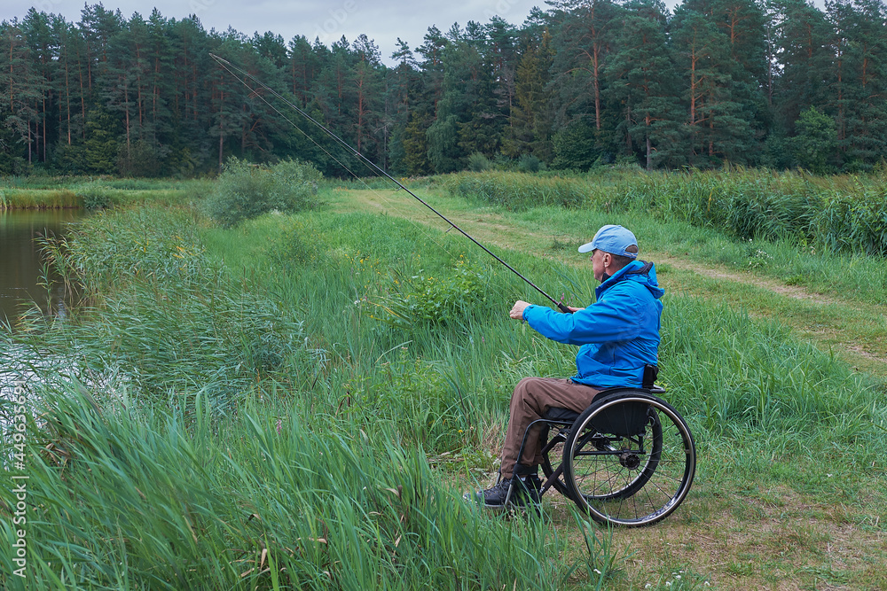 disabled man in a wheelchair and blue jacket is fishing on spinning rod on cloudy day disabled man in a wheelchair and blue jacket is fishing on spinning rod on cloudy day