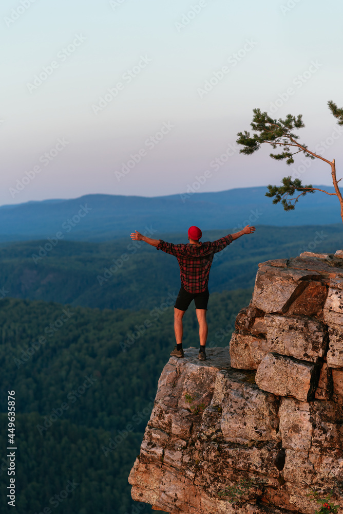 Obraz premium Back view of a man standing against the background of mountains with his arms outstretched. The man in the mountains raises his hands. Man on the background of mountains. Travel to the mountains