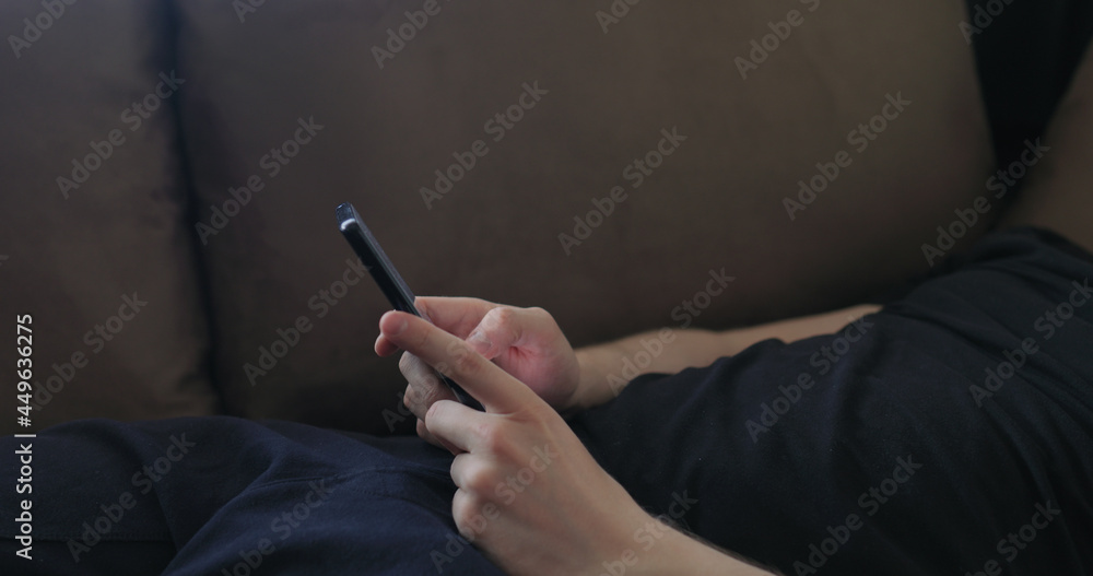 Closeup young man use smartphone working from home lying on couch side view Closeup young man use smartphone working from home lying on couch side view