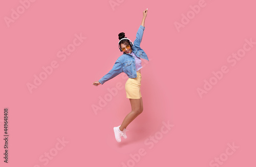 Fototapeta Naklejka Na Ścianę i Meble -  Happy beautiful Asian teen woman in yellow glasses listening music in headphones and dance on pink background..