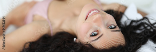 Smiling brunette woman lies on white bed