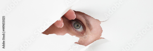 Female eye looks through hole in white paper