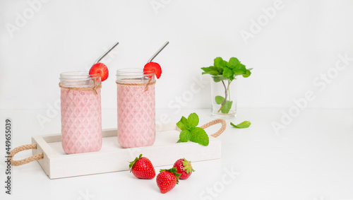 Fresh strawberry smoothie or milkshake with berries and mint on white wooden tray on white background. Top view. Healthy eating concept