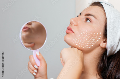 Facial lifting thread. Woman holding a mirror and show her cheak with arrows skin, contouring using mesothreads. Concept of plastic surgery photo
