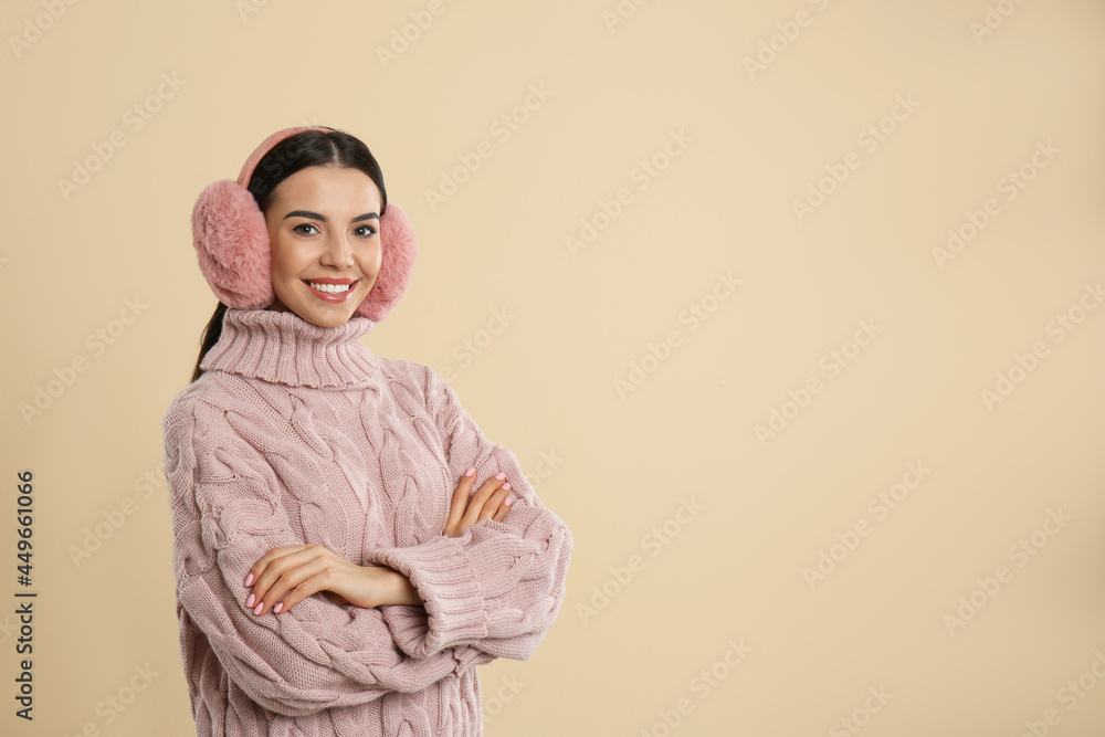 Beautiful young woman wearing earmuffs on beige background. Space for text Beautiful young woman wearing earmuffs on beige background. Space for text