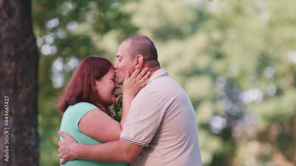 The happy husband gave flowers for his wife in the park and they are hugging each other with the flowers between them. The happy husband gave flowers for his wife in the park and they are hugging each other with the flowers between them.