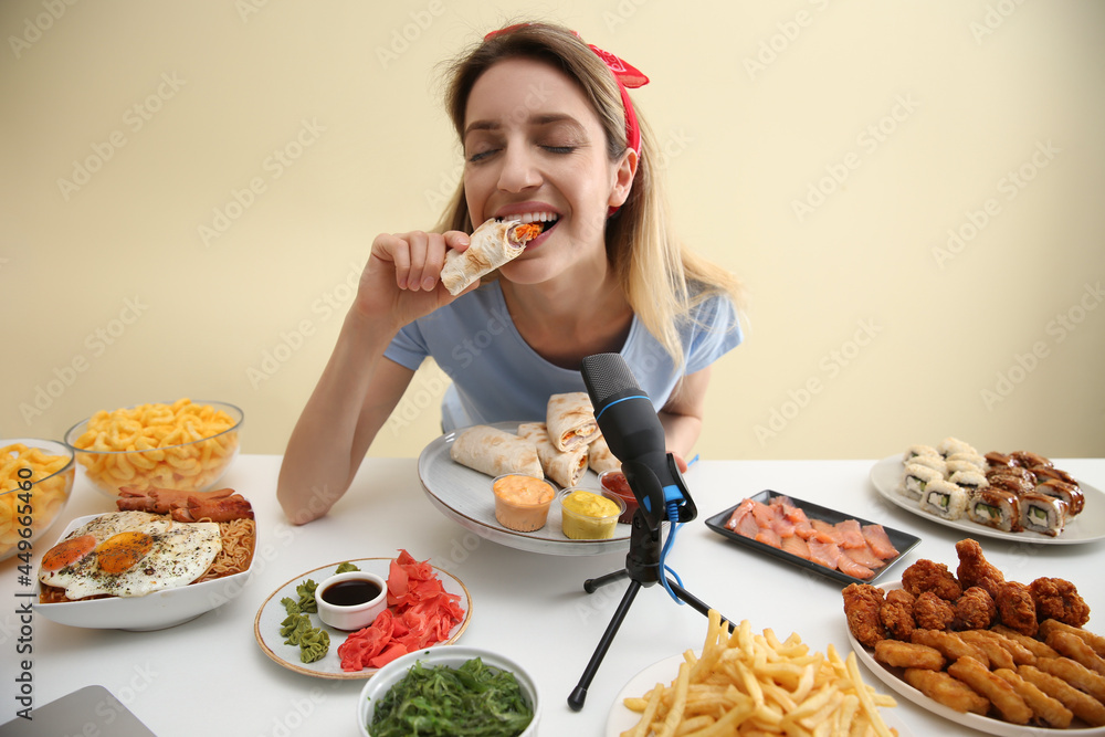 Food blogger eating in front of microphone at table against light background. Mukbang vlog Food blogger eating in front of microphone at table against light background. Mukbang vlog