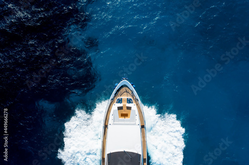 View from above, stunning aerial view of a luxury yacht cruising on a blue water with waves crashing on the bow of the boat. Costa Smeralda, Sardinia, Italy.