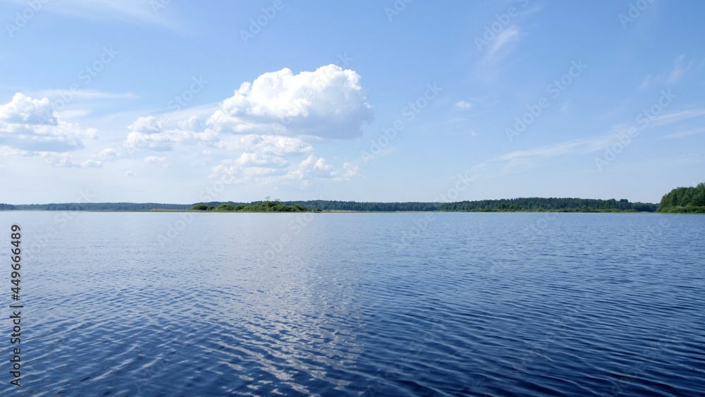 Beautiful landscape. Big blue lake. White clouds in the blue sky. Sunny summer weather. Island with many green trees.