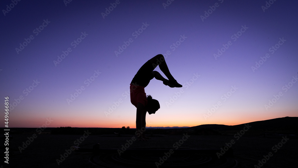 silhouette of a teenage girl doing gymnastics and jumping jacks at sunset.
