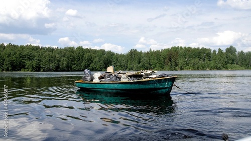 A boat full of garbage floats on the lake. Waste transportation. White clouds in the blue sky. Sunny summer weather. Waste for recycling. Cleaning forests and islands. Environmental protection
