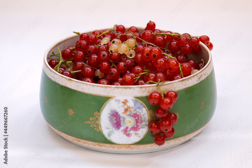 Red currant and white currant fruits with branches in a vase against a white background by summer day Red currant and white currant fruits with branches in a vase against a white background by summer day