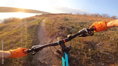The cyclist rides a technical rocky trail along the river into the sunset. First-person view.