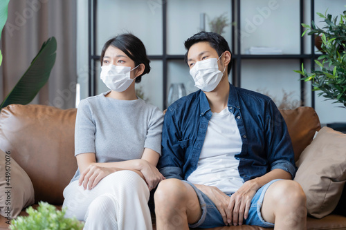 portrait of young asian adult male and female wear face mask protective from covid epidemic home isolation distance at home,quarantine people in apartment looking out of window